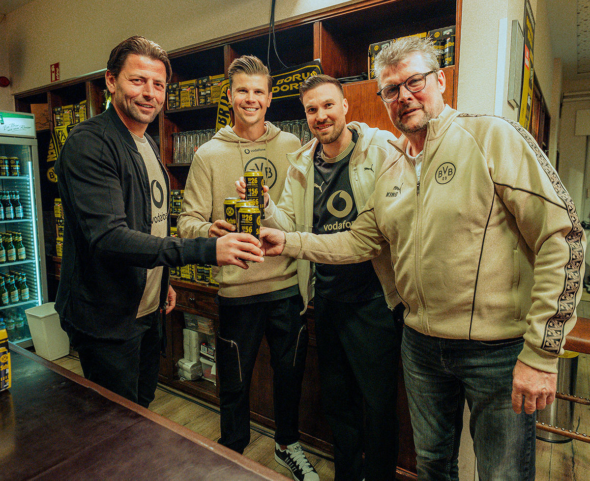 Vier Männer stoßen mit mit Dosenbier an, im Hintergrund ein Regal mit Brinkhoffs Gläsern. 