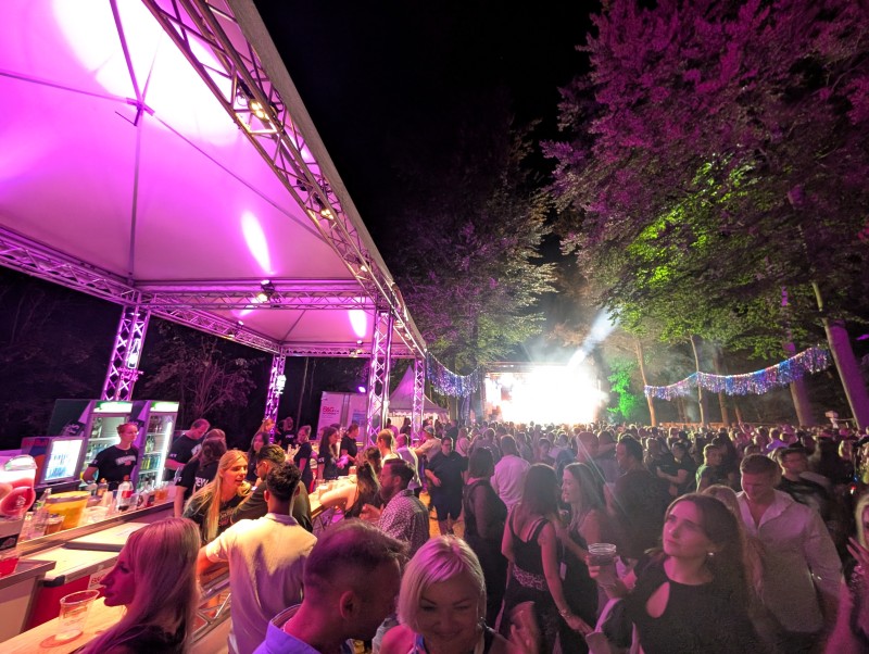 Feiernde Menschenmenge neben einer Open-Air Bar, im Hintergrund eine beleuchtete Bühne