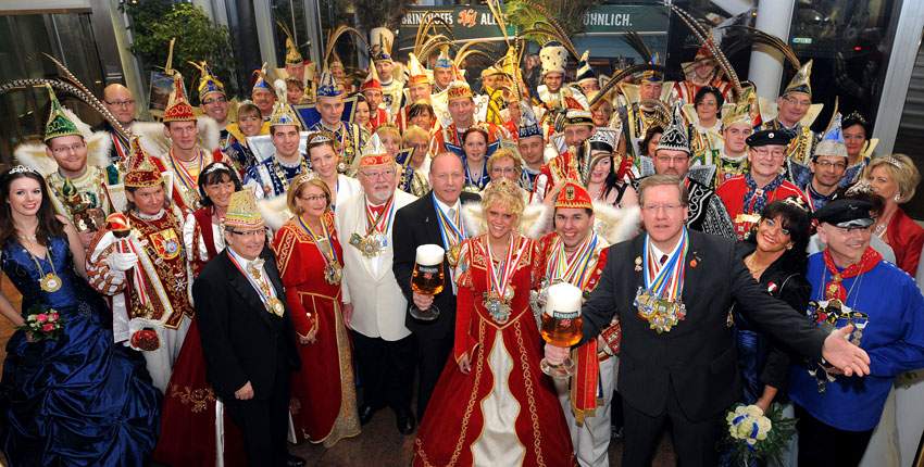 Eine Gruppe von Personen in farbenfrohen Karnevalskostümen posiert mit Bierkrügen.