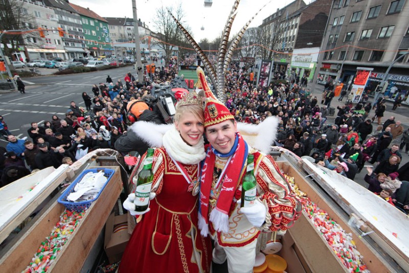 Zwei Personen in traditioneller Karnevalskleidung stehen auf einem Wagen und lächeln.
